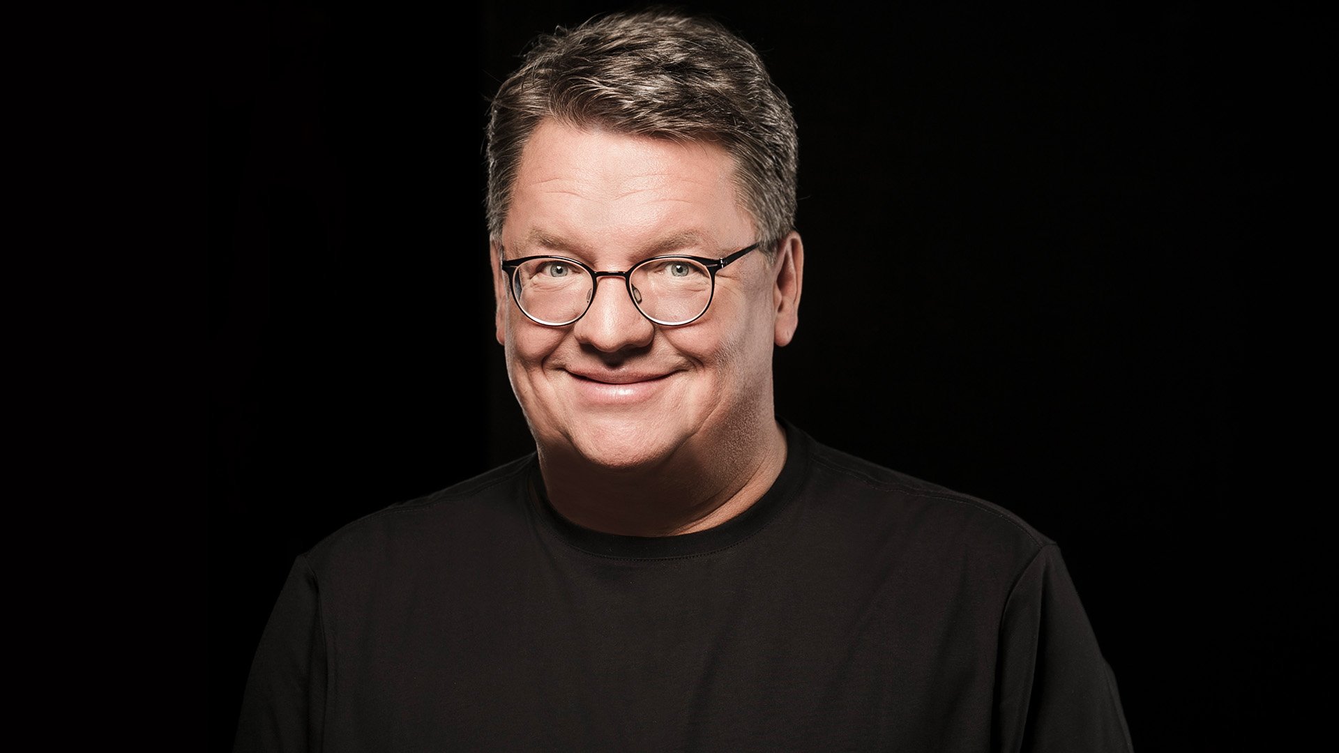 Porträt von Helmut Schleich mit Brille vor schwarzem Hintergrund.