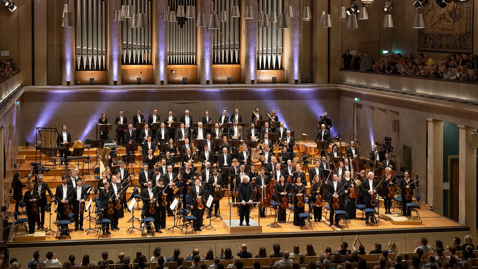 Foto von einem Orchester und dem applaudierenden Publikum.