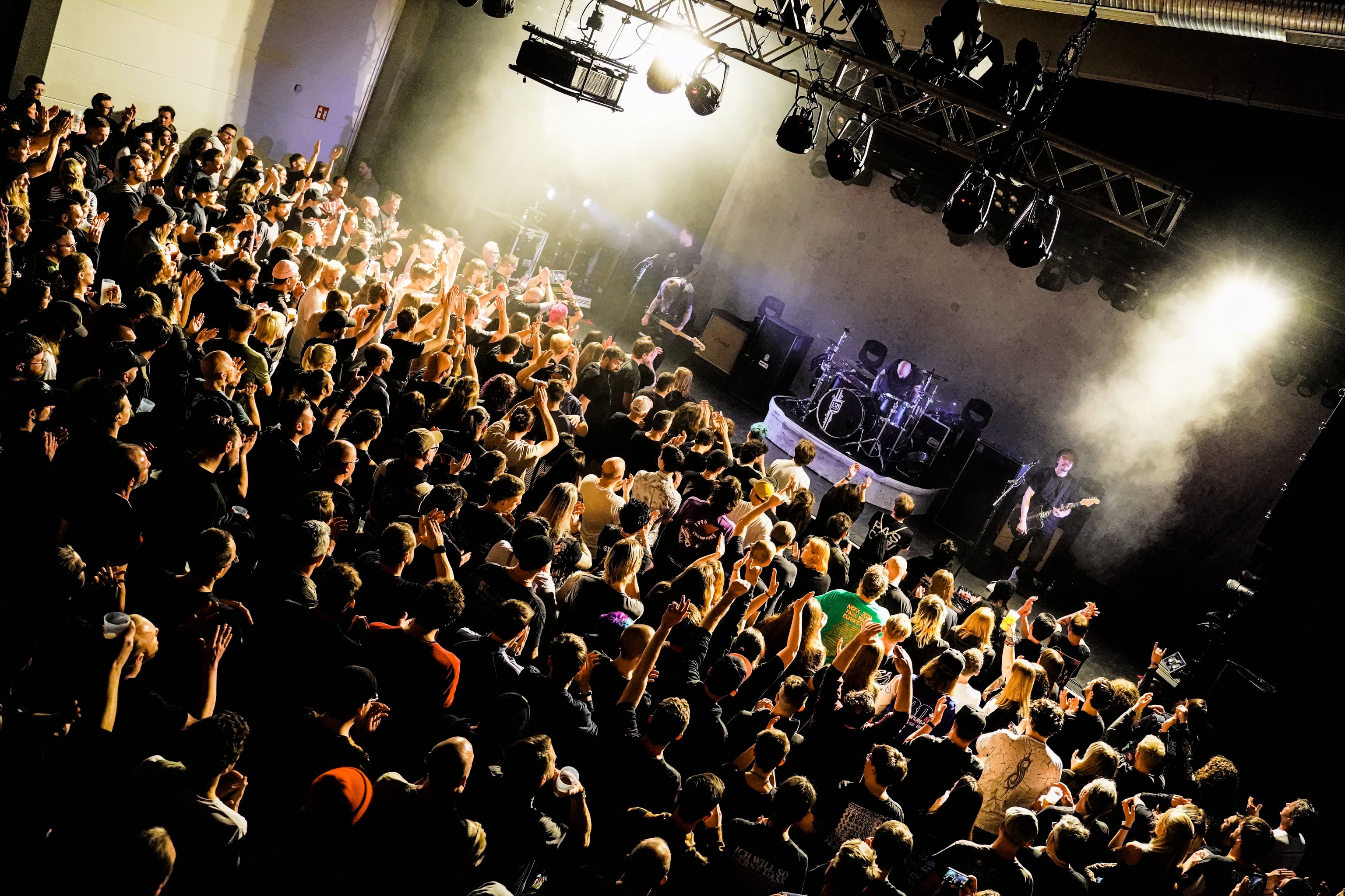 Eine Crowd mit vielen Menschen vor einer Bühne. Auf der Bühne eine Band während ihres Auftritts.