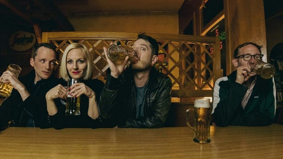 Foto für die Veranstaltung von Hovacek: An der Bar sitzen drei Männer und eine Frau und trinken Bier