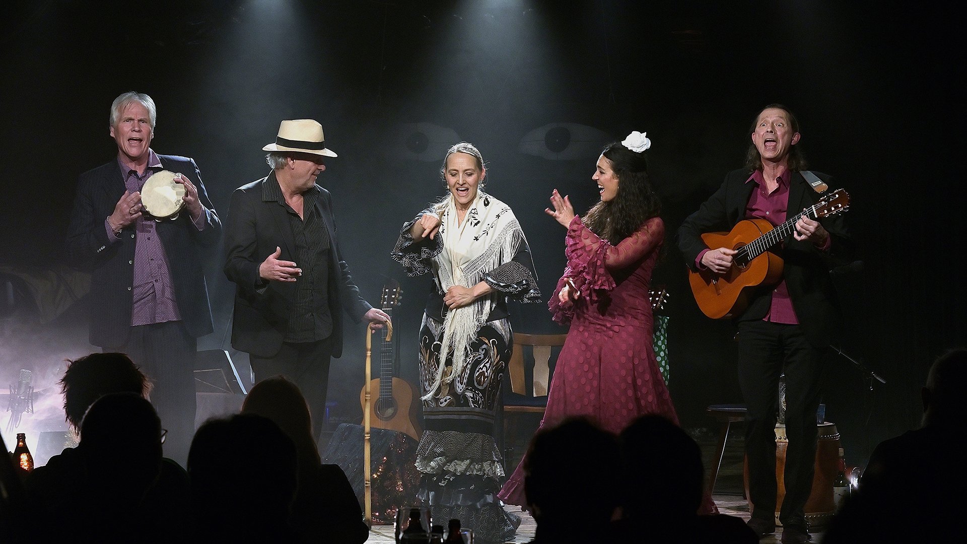 Fünf Musikerinnen und Musiker singen und musizieren auf einer Bühne mit Gitarre, Tamburin und Flamencoelementen vor Publikum.