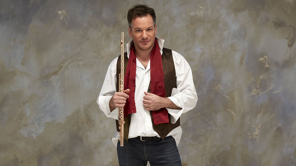 Emmanuel Pahud, der Soloflötist der Berliner Philharmoniker mit Querflöte in der Hand, weißem Hemd mit offenem Kragen, dunkle Weste roter Schal, marmorierter Hintergrund in Beige und Grau