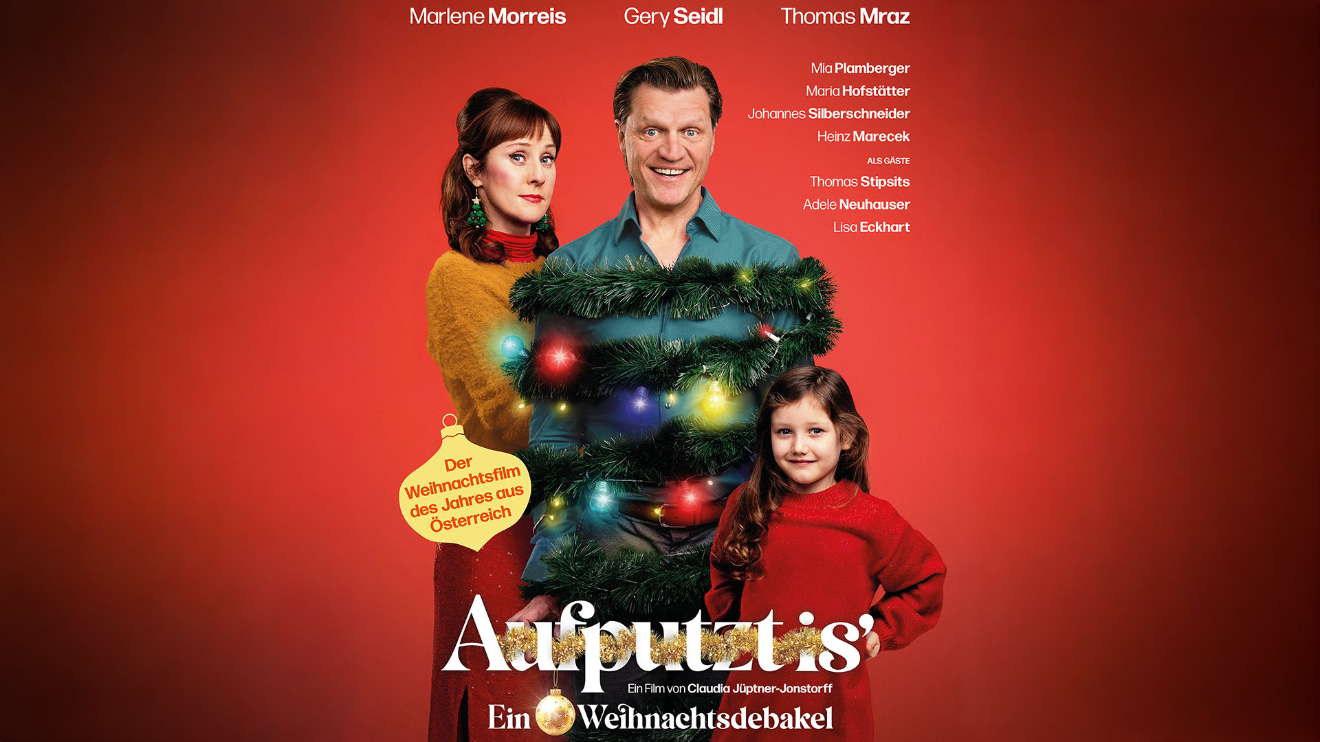 Plakat Aufputzt mit drei Personen vor rotem Hintergrund, eine Figur mit Weihnachtsgirlande und bunten Lichtern geschmückt in der Mitte, daneben zwei weitere Personen in farbiger Kleidung, darunter großer Titel Aufputzt und Zusatz Ein Weihnachtsdebakel