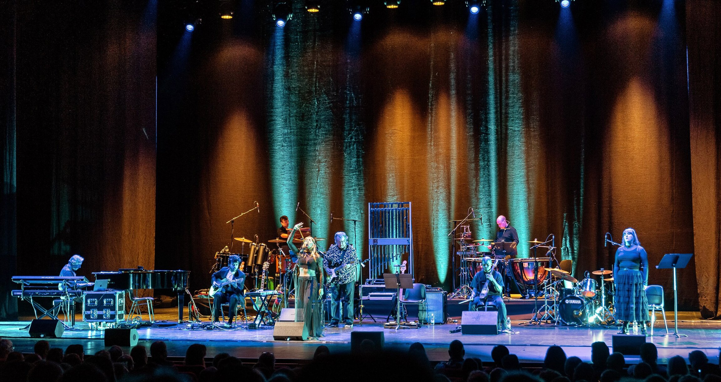 Foto der Künstlerin bei einem Konzert auf der Bühne mit ihren Musikern und Instrumenten