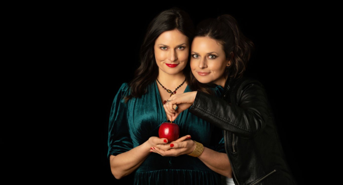 Foto von zwei Frauen, eine davon mit einem grünen Kleid und einem Apfel vor schwarzem Hintergrund
