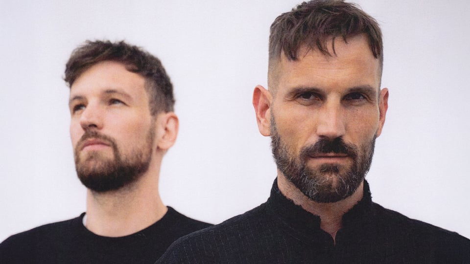 Portrait der beiden Künstler in schwarzer Kleidung mit hellem Hintergrund