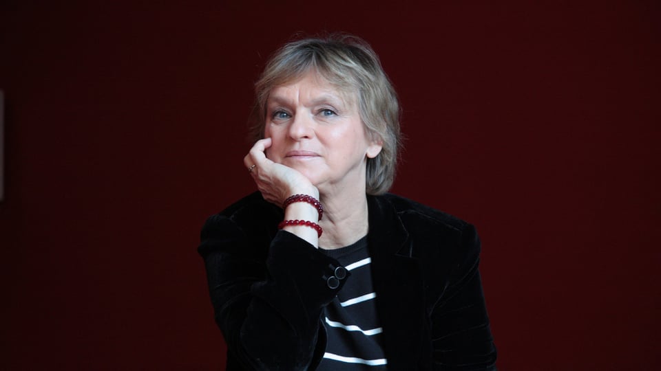 Foto für die Veranstaltung Elke Heidenreich – Ach, eine Fanfare! mit der Künstlerin vor einem bordeauxfarbenen Hintergrund.