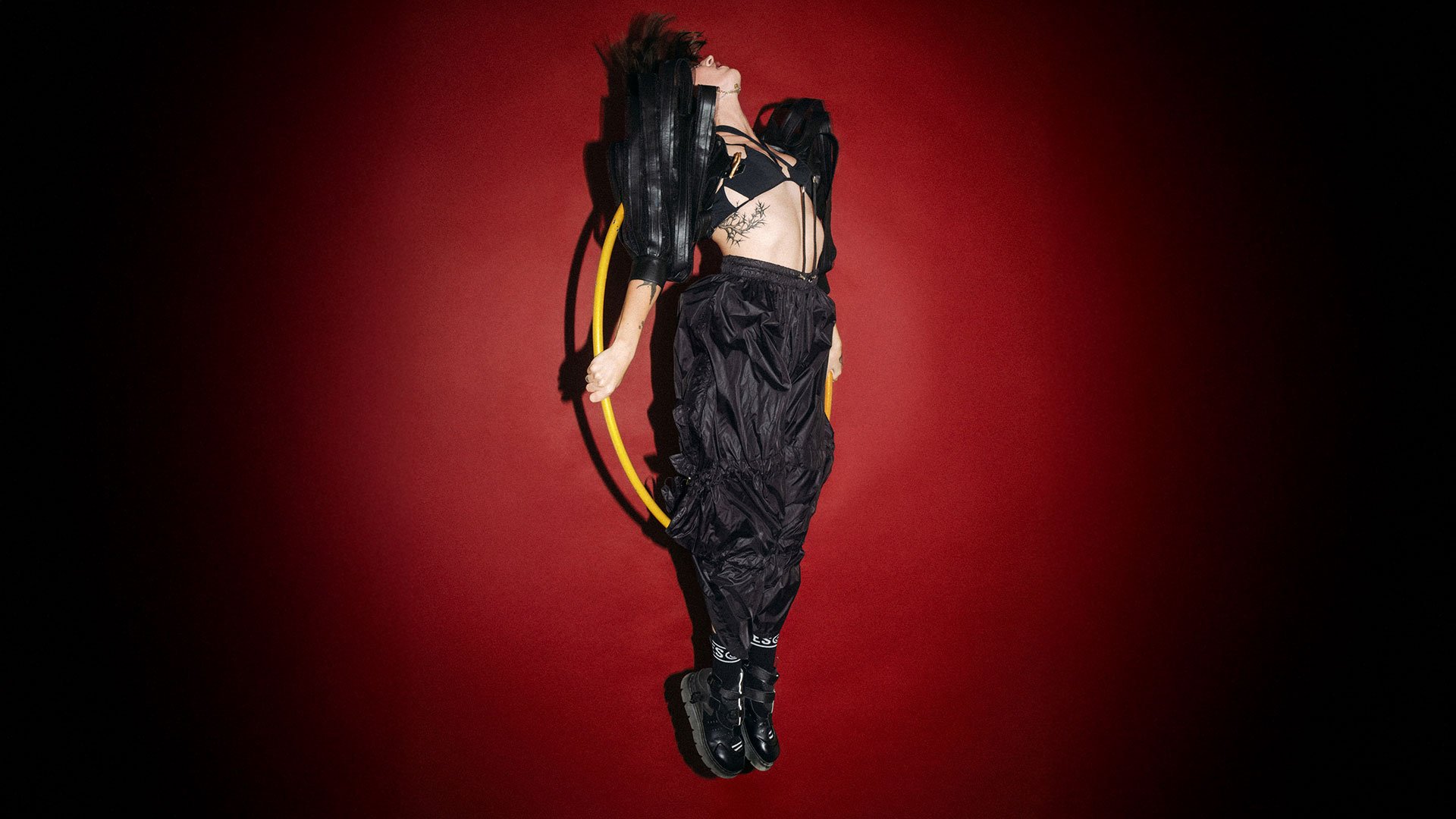 Foto für die Veranstaltung „MINE – Tour 2026“ mit der Künstlerin in Schwarz mit Hula-Hoop vor rotem Hintergrund.