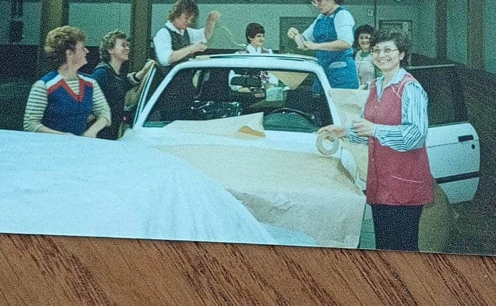 Ein altes Foto auf einem Holztisch, auf dem Frauen und ein Auto zu sehen sind