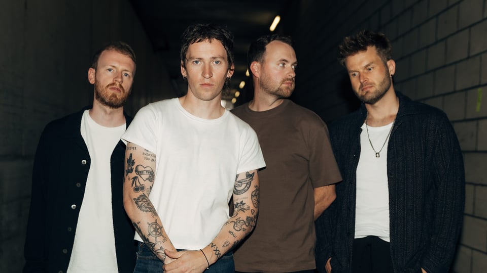 Die vier Musiker der Band stehen in einem Flur mit seitlich weiß gekachelten Wänden