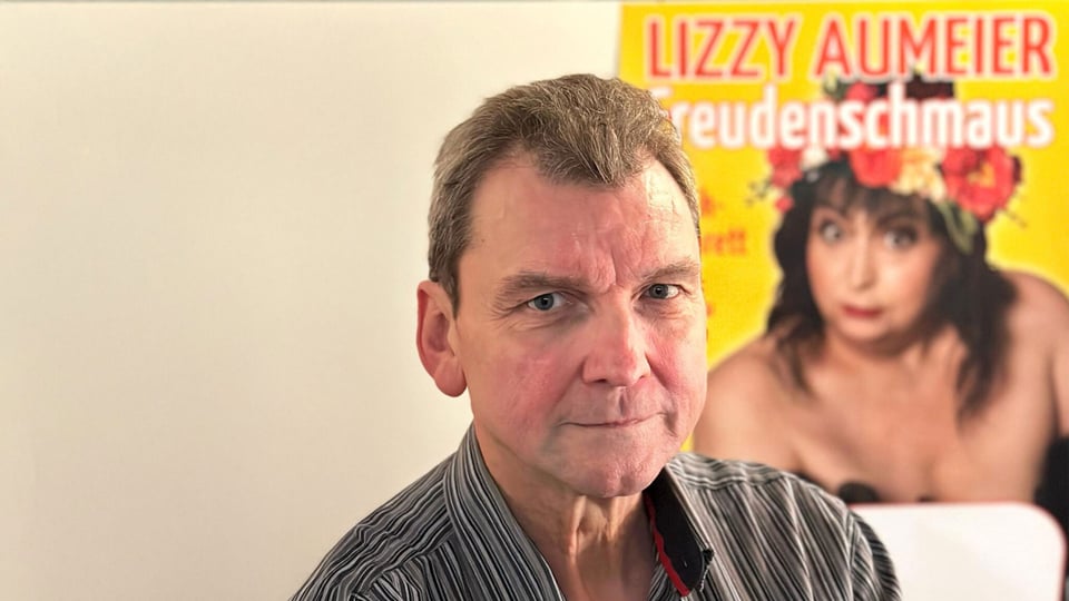 Foto für das Event von Andreas Stock mit dem Künstler und im Hintergrund einem Poster der verstorbenen Lizzy Aumeier