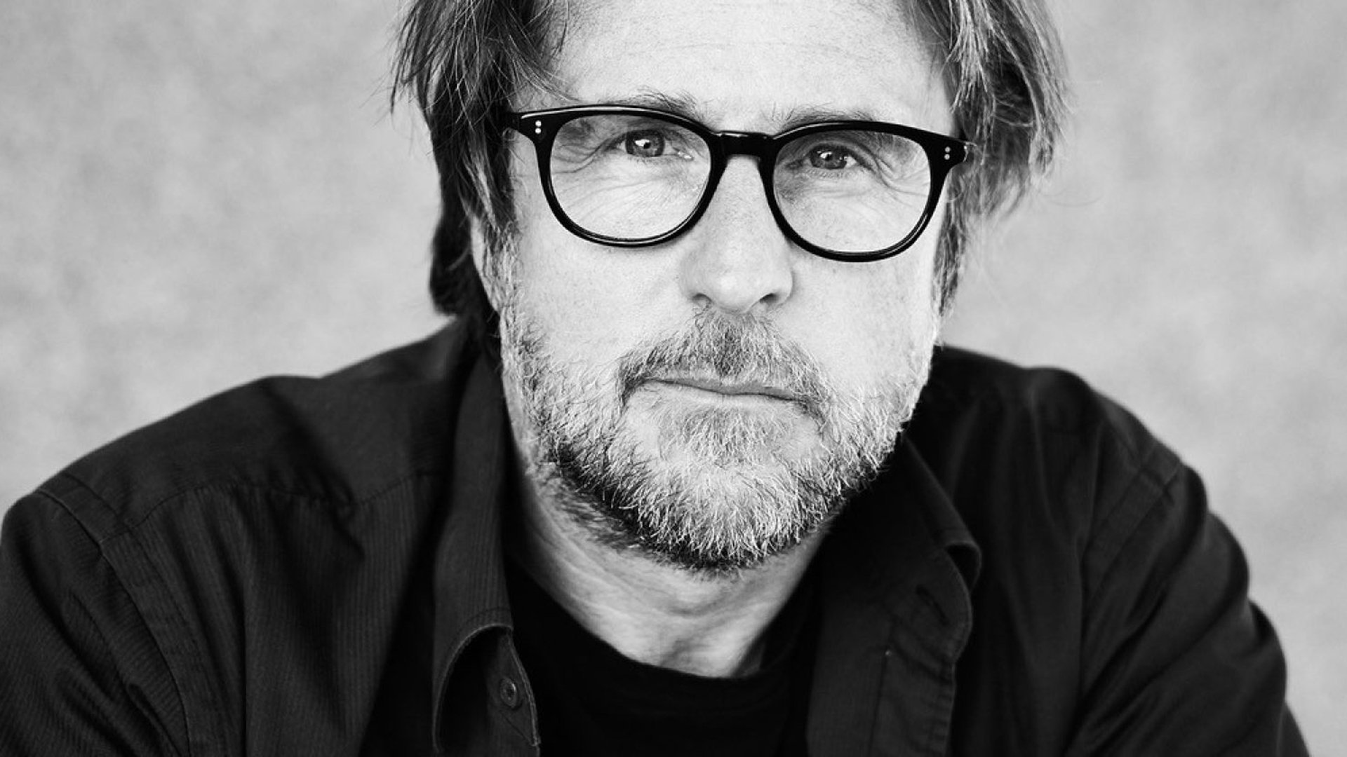 Ein schwarz/weiss Foto des Schauspielers Bjarne Mädel in dunklem Hemd und Brille