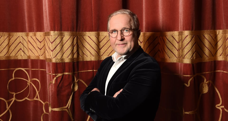 Mann vor einem rot-goldenen Vorhang