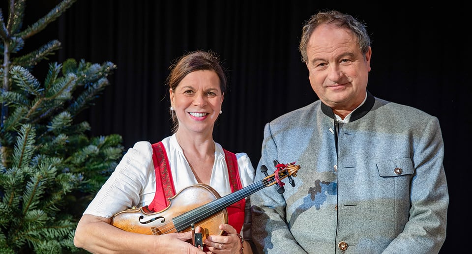 die beiden Künstler mit einem Instrument und einem Weihnachtsbaum auf der linken Seite, auf schwarzem Hintergrund