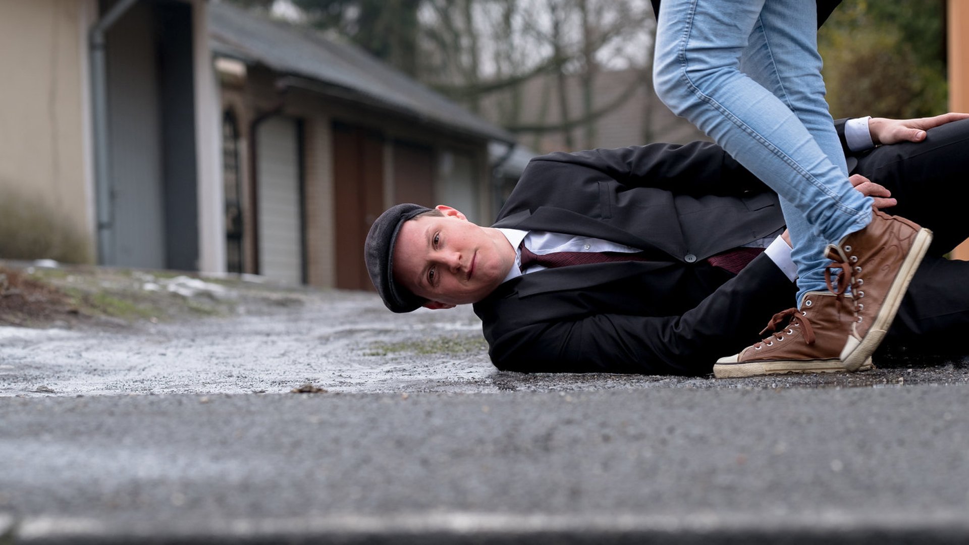 Mann liegt auf der Straße und schmunzelt davor sieht man ein paar Schuhe und Füße einer anderen Frau