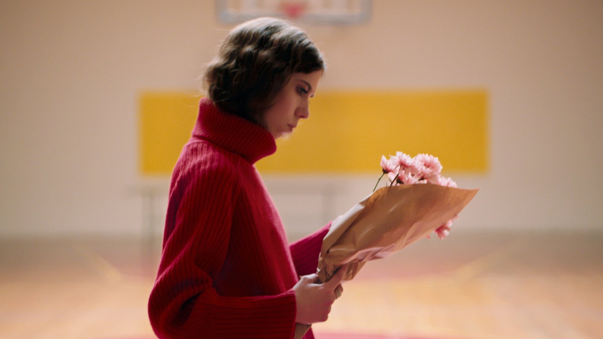 Ein Foto für das Event „KILLERWOOD“ bei der Griechischen Filmwoche München: Eine Frau mit rotem Pullover hält einen Blumenstrauß in den Händen.