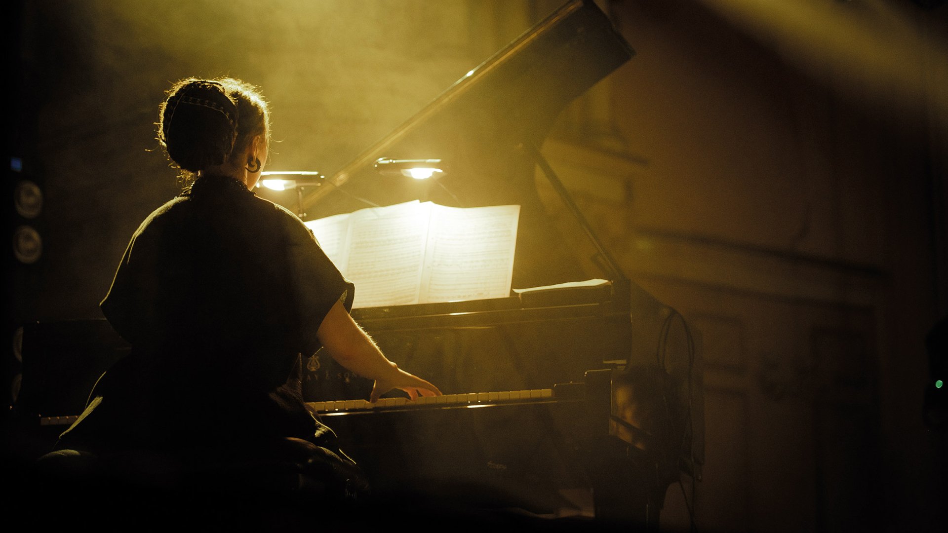 Die Künstlerin von hinten an einem Konzertflügel in Dämmerlicht