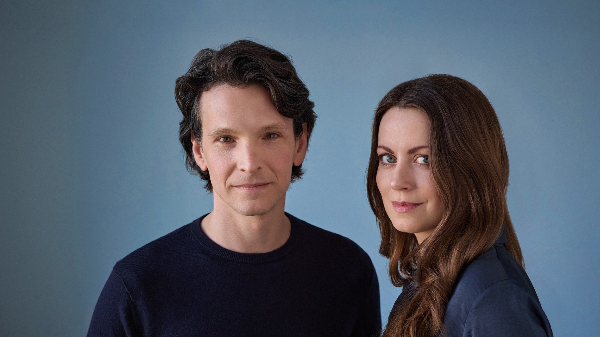 Sabin Tabrea und Alice Dwyer lächelnd  in dunkler Kleidung vor blauem Hintergrund