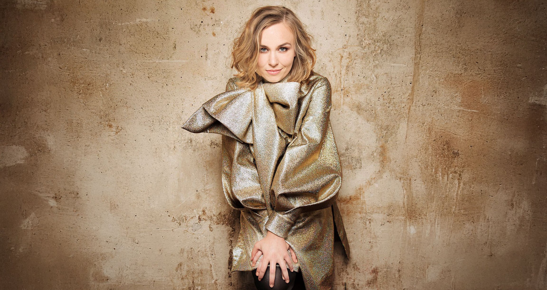 Blonde Dame in gold glänzender Kleidung vor hellem Hintergund