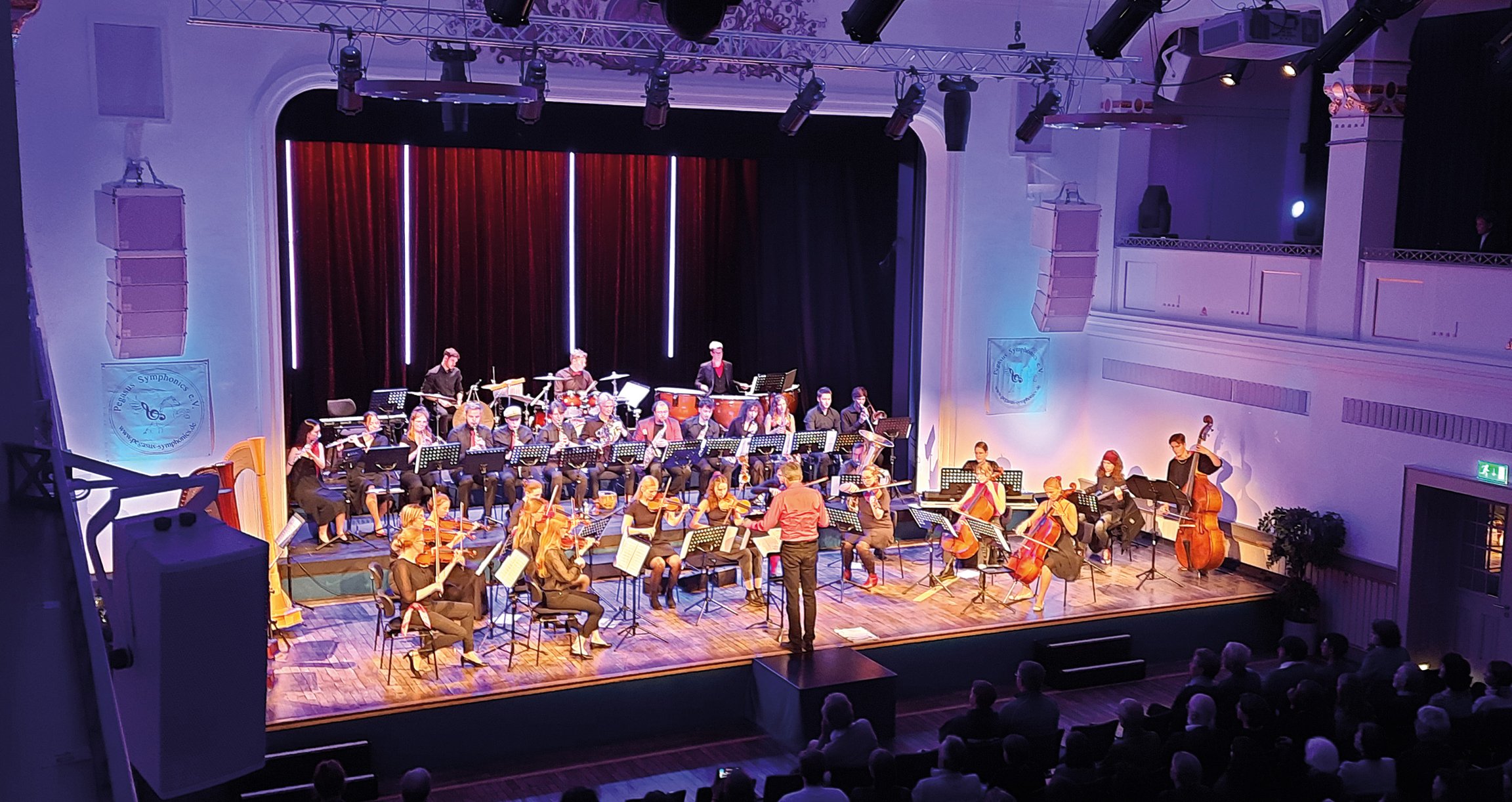 Foto des Orchesters auf der Bühne und des Publikums.