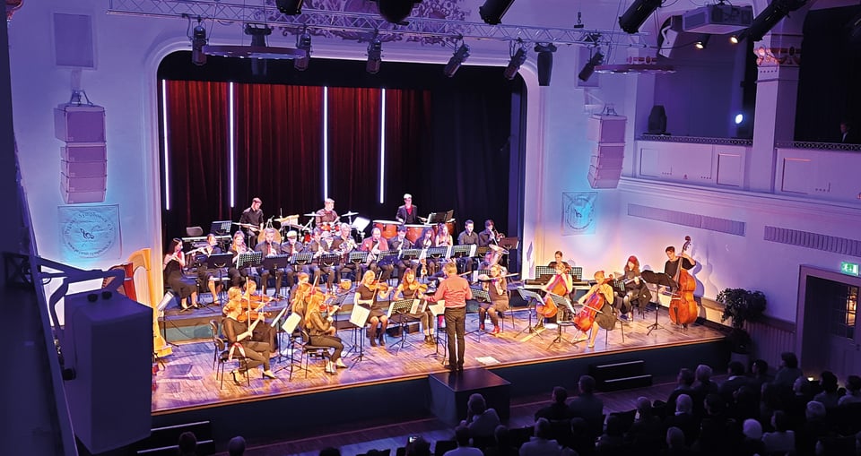 Foto des Orchesters auf der Bühne und des Publikums.
