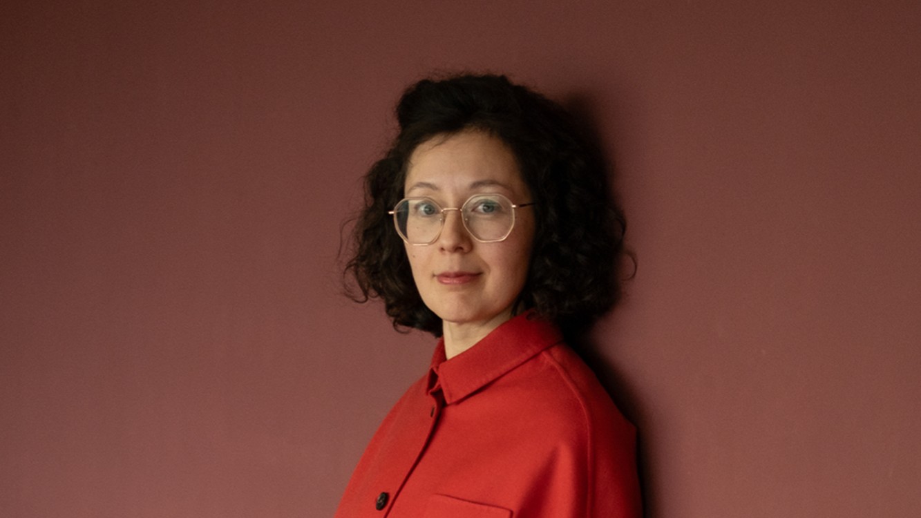 Yuko Kuhn in oranger Bluse vor rotbraunem Hintergrund