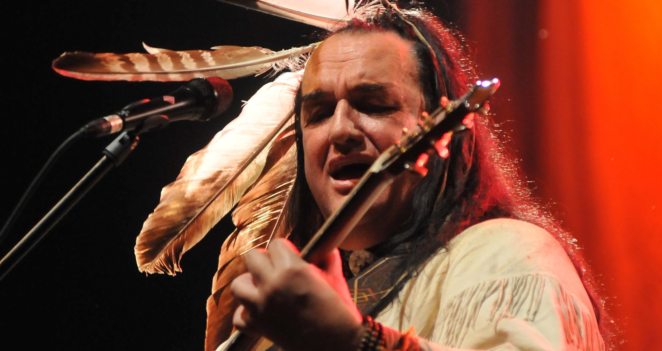 Mann mit langen Haaren und Federn mit Gitarre
