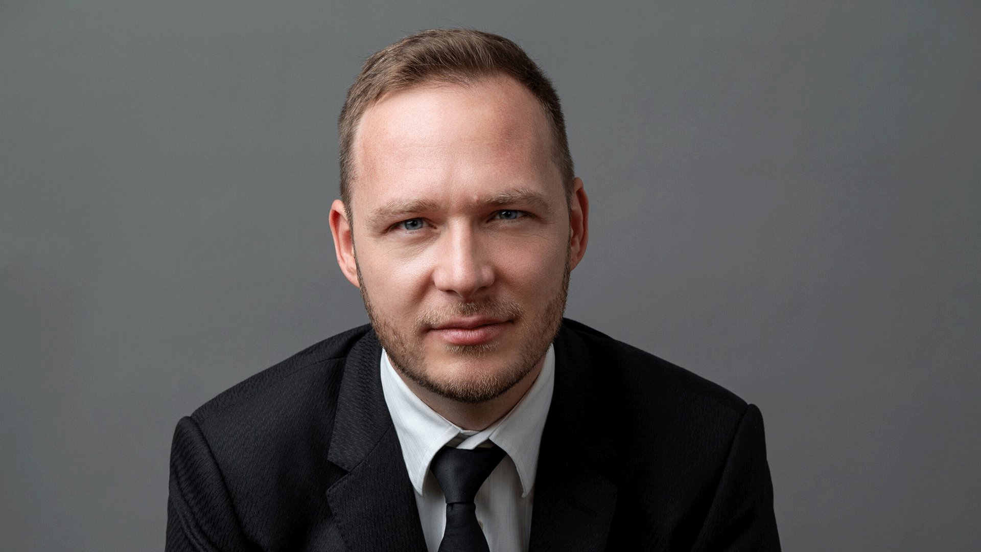 Ein Portrait von Andre Herrmann vor grauem Hintergrund mit einem geraden Blick in die Kamera
