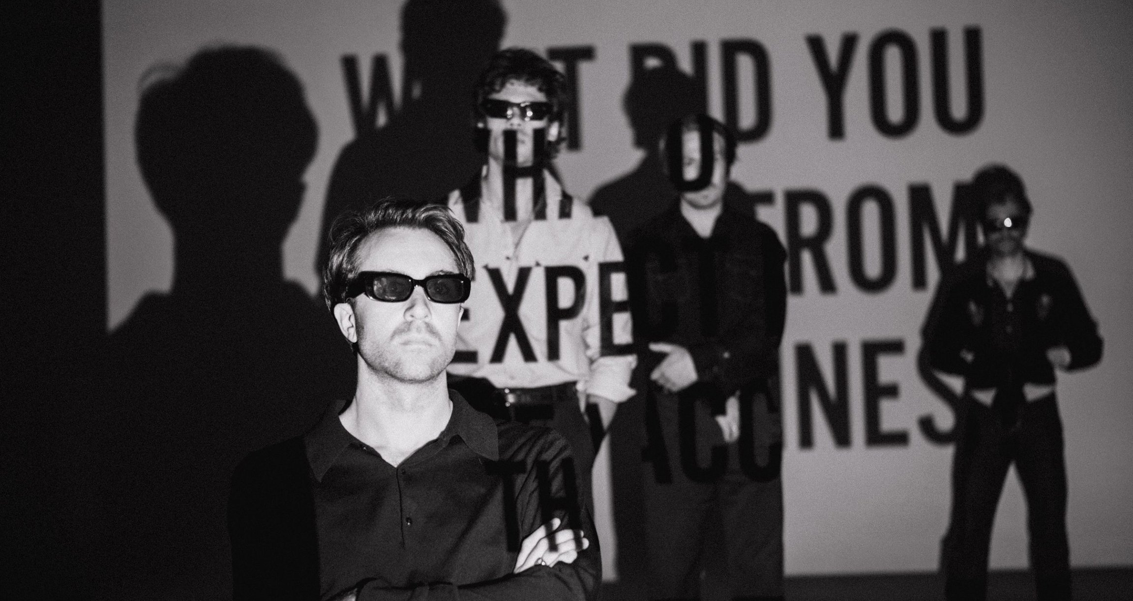 schwarz weiss Bild der Band mit projizierter Schrift
