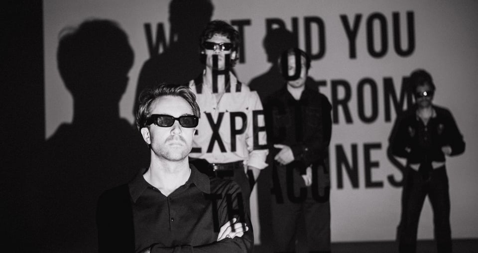 schwarz weiss Bild der Band mit projizierter Schrift