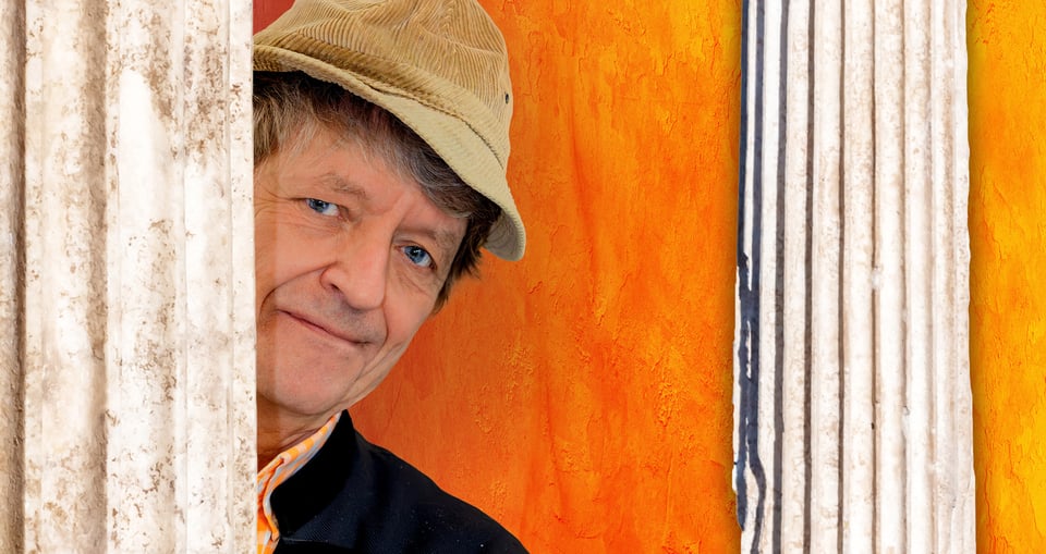 Mann mit beiger Cordmütze vor orangem Hintergeun