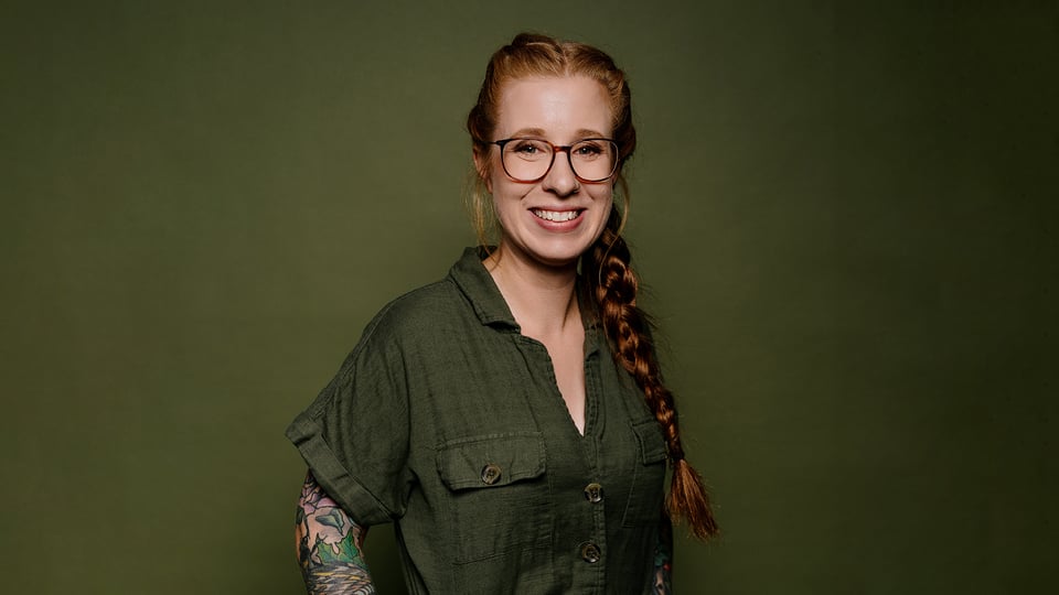 Die Künstlerin mit Zopf in grüner Bluse vor grünem Hintergrund