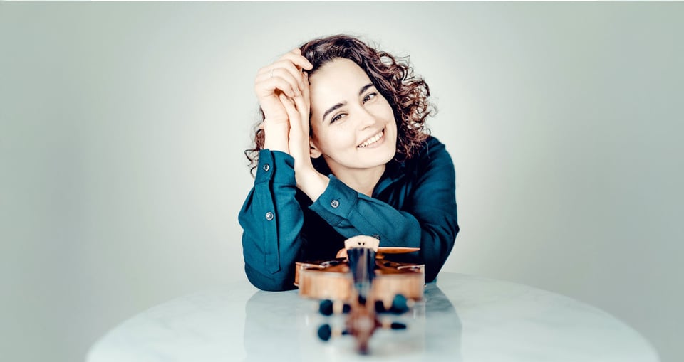 Alena Baeva lächtelt in die Kamera mit ihrer Violine im Vordergrund