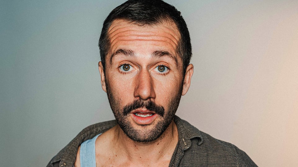 Foto für die Veranstaltung „Stefan Leonhardsberger – Herzklopfen“, mit dem Künstler vor einem Hintergrund in Blau-Beige-Verlauf.