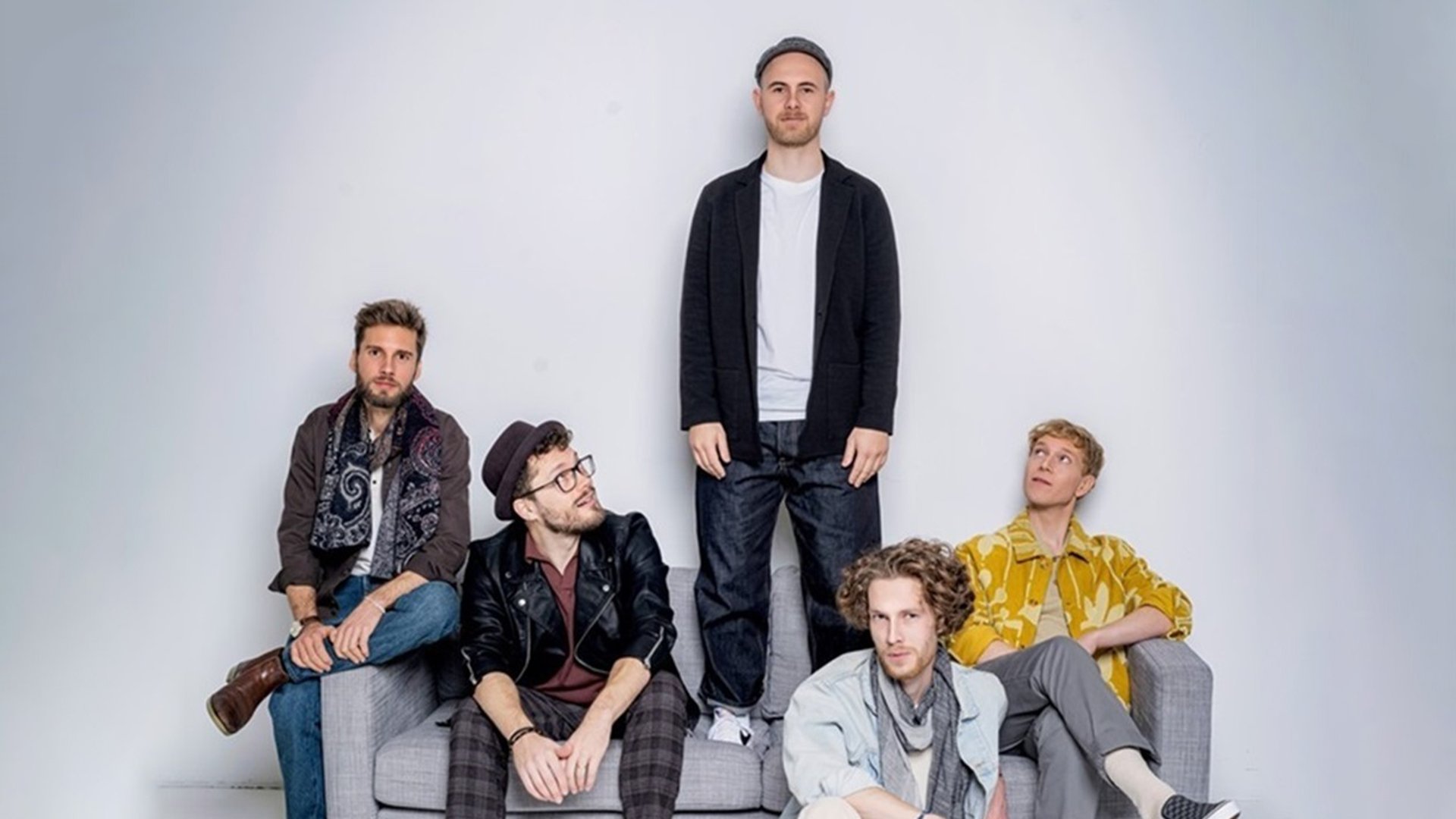 Die fünfköpfige Band auf einem grauen Sofa mit grauem Hintergrund