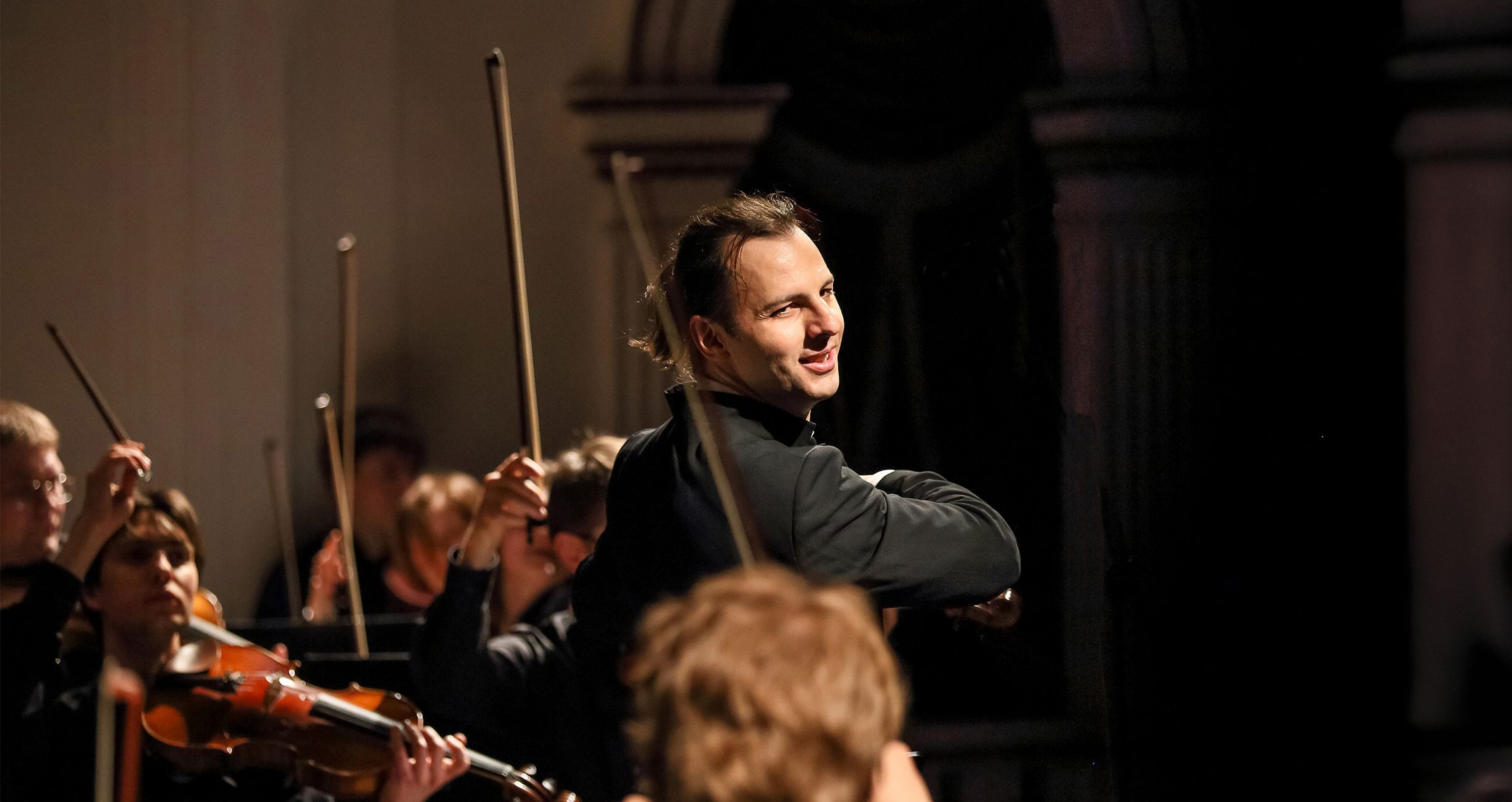 Mann in schwarzem Hemd und Instrumen mit Orchester im Hintergrund