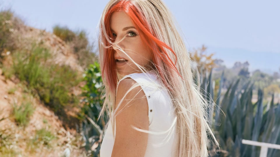 Foto für die Veranstaltung von TAYLOR ACORN mit roten Strähnen im Haar und einer Landschaft im Hintergrund