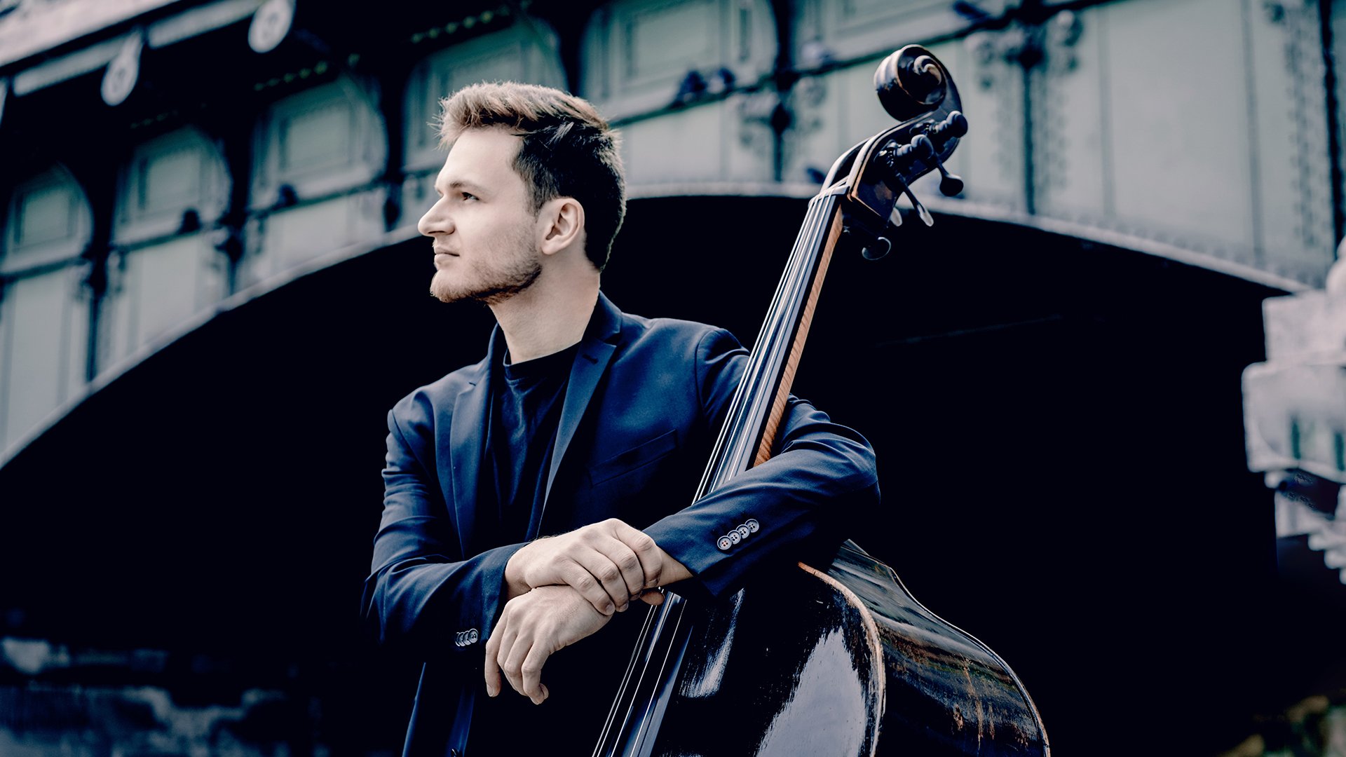 Dominik Wagner lehnt an einem Kontrabass. Im Hintergrund spannt eine Brücke.